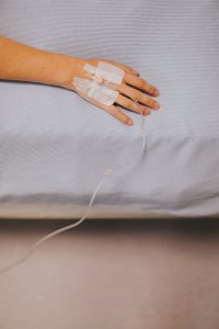 A caucasian hand with an IV in it on a bed.