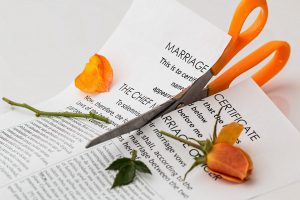 Scissors cutting through a piece of paper that says marriage of certificate and an orange rose on top of the paper.