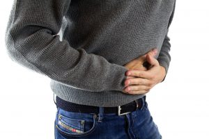 Caucasian male's torso with a gray sweater, and both hands holding stomach.