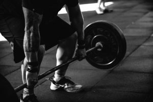 Man's body squatting down to lift bar with large weights on. 