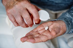 Older caucasian man's hand dropping a pill onto his palm from a pill bottle.