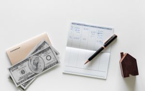 Two hundred dollar bills next to an open checkbook with a pen on it.
