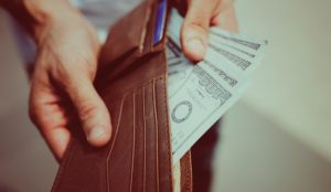 Caucasian hands holding a wallet, with one hand holding hundred dollar bills out of it.