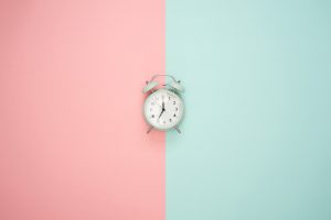 White clock in between two colored walls, on the left pink and the right light blue.
