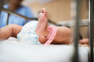 Caucasian baby's legs on hospital bed with diaper on, and pink band around left ankle.