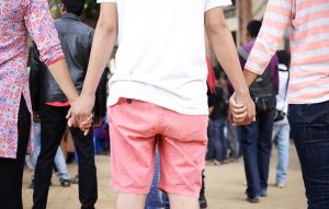the back of three people. A man in the middle holding hands with women on each side of him.