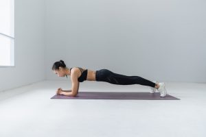 Caucasian woman dressed in black sports bra and black leggings doing a plank.