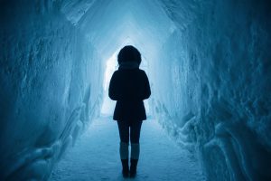 Woman dressed in a winter coat walking through a tunnel of snow.