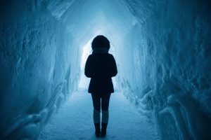Woman dressed in a winter coat walking through a tunnel of snow.