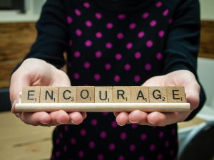 the word encourage spelled out with scrabble pieces being help by a little girl's hands.