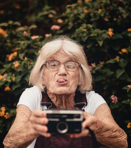 Older white caucasian woman holding a camera up while sticking out her tongue.