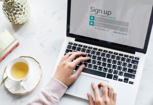 laptop on a table with two hands on it and "sign up" on the laptop screen.