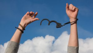 Caucasian hands with a set of handcuffs on oe and the other free of it.