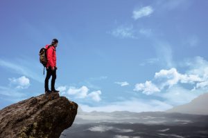 Caucasian man standing at the top of a mountain peak.