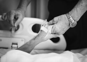 Black and white picture of two caucasian hands holding each other. One in a hospital bed.