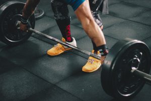 Caucasian man's legs on the groun and arms on a barbell with weights.