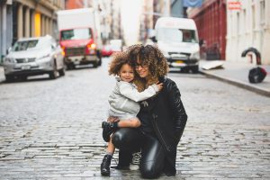 Caucasian woman with curly hair bending down and holding a little girl with curly hair.