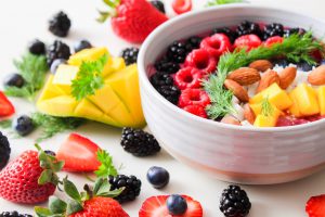 White bowl filled with fruits and nuts surrounded by more fruit on the table, for psoriasis diet.