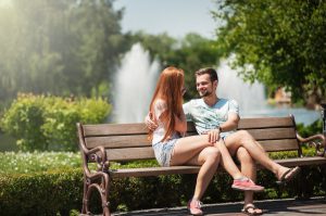 Young caucasian man and woman sitting on a park bench talking.