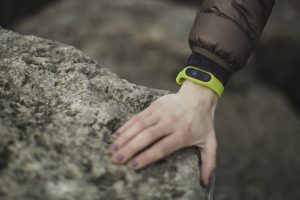 Caucasian woman's hand on a rock with a green fitness tracker on her wrist.