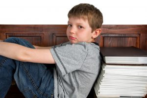 Caucasian little boy sitting on a bench with his back against some books.