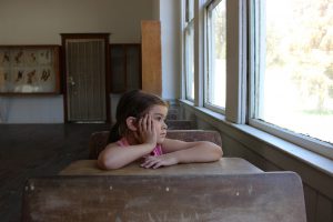 Caucasian little girl sitting at school desk looking out of the window.