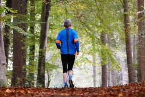 Caucasian man with gray hair running in a trail with a blue shirt on and black leggings.