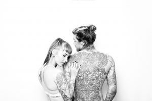 Caucasian woman grabbing a caucasian man's arm and back that is covered in tattoos.