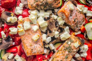 Cooked salmon laying on a bed of tomatoes with mushrooms and cheese on top.