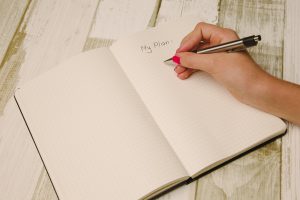Caucasian woman;s hand holding a pen ready to write on an openedbook with the page titled "my plan."