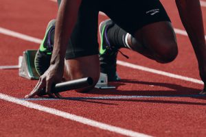 Legs of an African American man with a bar in his hand bent down reeady to run.