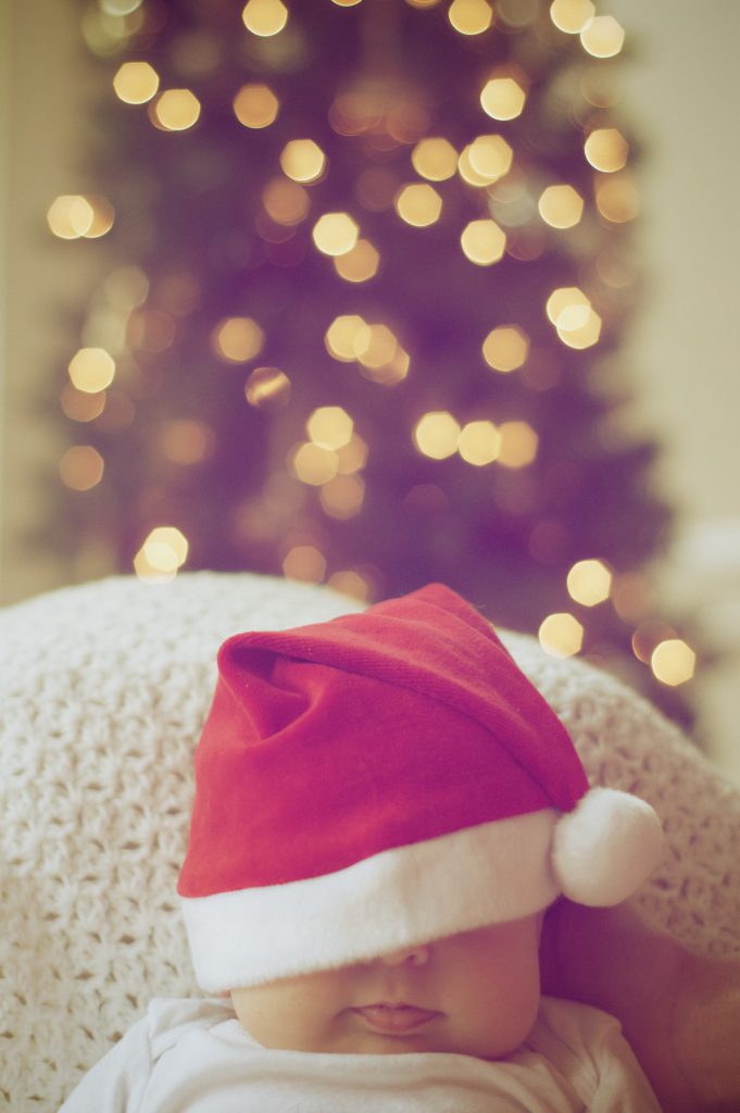 baby with santa hat with a lit tree in the background