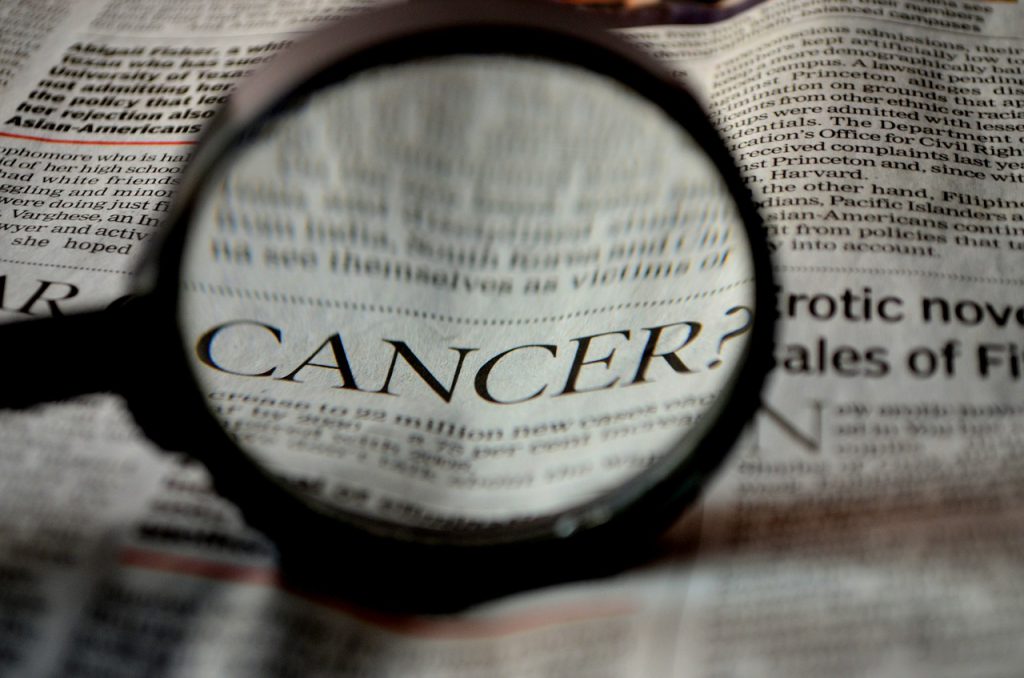 the word "cancer" in a newspaper article magnified by a magnifying glass 