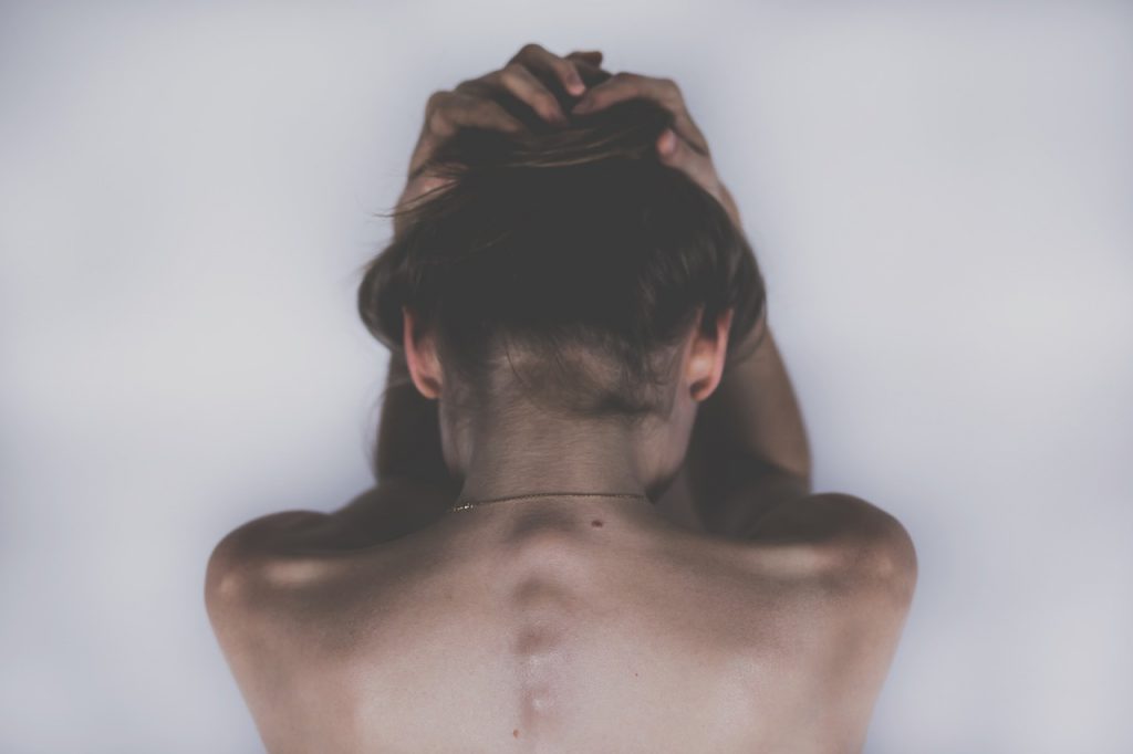 Caucasian womans bare back holding her hair up while looking down