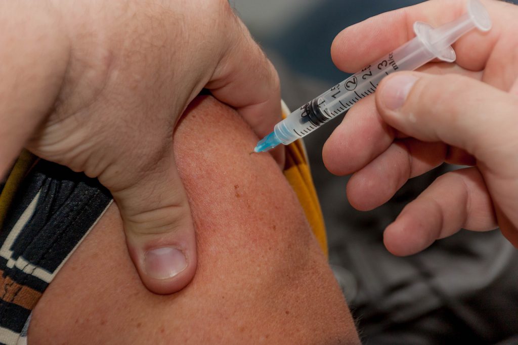 A person sitting down getting a shot in their upper arm. 