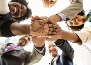 A group of employees standing in a circle with their hands on top of one another. Camera view is looking up at their palms.