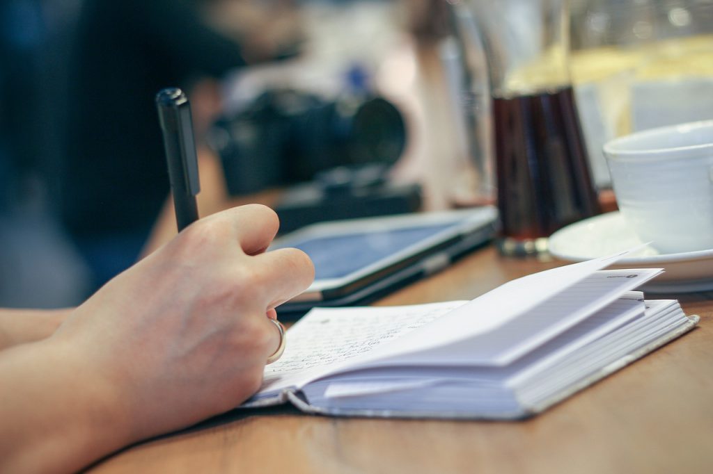 Hand writing with a pen into a book on a wooden table.