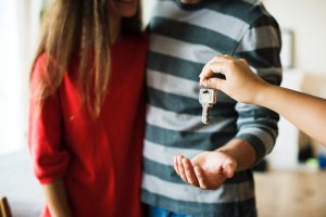 Couple stanging next to each other with the man's hand out about to take a key from another hand that is giving it.