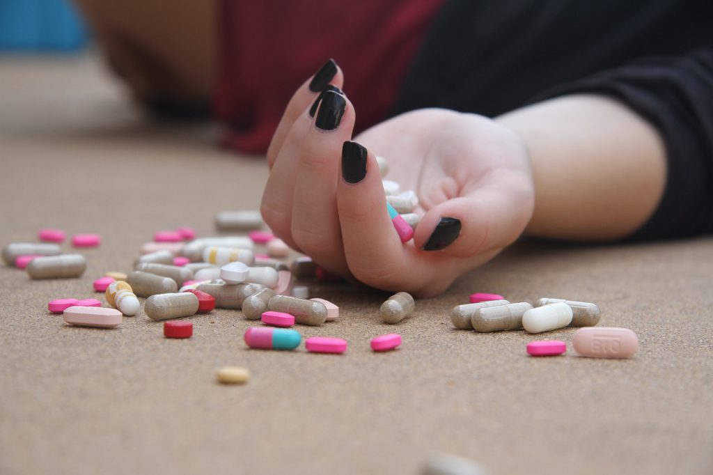 Caucasian womand hand on the ground with pills in the palm and pills laying on the floor next to her hand. 