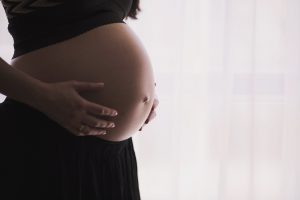 Woman's pregnant belly being held with both hands.