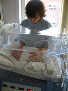 Caucasian woman with a light blur robe ontouching a baby in a NICU basket