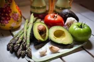 Avocado, asparagus, red tomato, green tomato, and garlic cloves on cutting board.