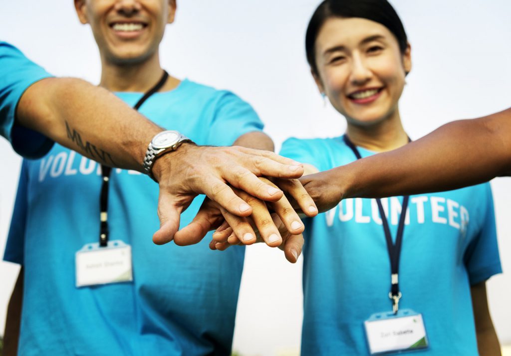 Asian woman and caucasian man with blue shirts on that say "volunteer" putting their hands in a huddle.