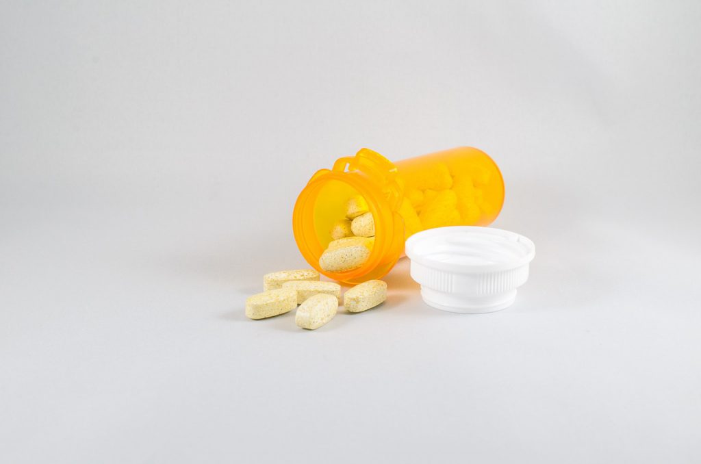 An orange pill bottle laying on a white table, open with white pill falling out of it. 