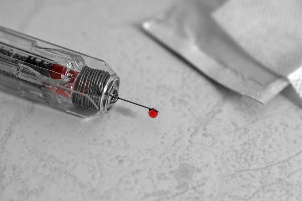 Needle point with blood on the tip laying on top of a white counter.