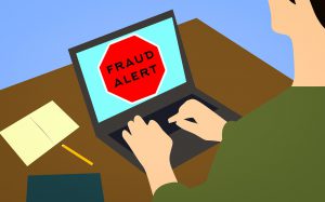 cartoon of a person sitting in front of a laptop with "fraud alert" on the screen