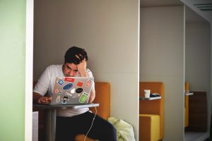young man frustrated with his hand in his hair looking at his laptop.