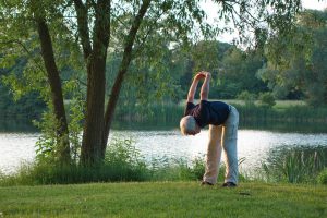 Older man with white hair in the park bending over with hands behind back