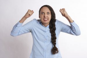 Caucasian woman with a light blue buttin up and braid on the side of her body, with her fists up angry.