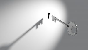 silver key going towards a lock in a white wall.